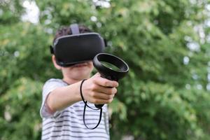 A seven-year-old boy in virtual reality glasses plays outside in the park. Children using technology. selective focus photo