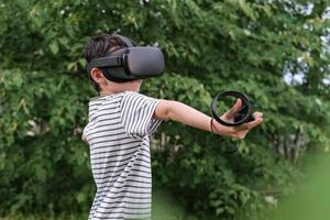 A seven-year-old boy in virtual reality glasses plays outside in the park. Children using technology photo