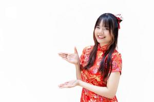 hermosa y bonito joven asiático niña con largo pelo quien usa un rojo cheongsam vestir en chino nuevo año tema mientras ella muestra su mano a presente alguna cosa aislado en blanco antecedentes. foto