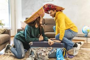 joven Pareja vistiendo sombrero es preparando el maletas para el siguiente viaje foto