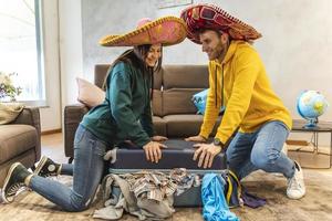 joven Pareja vistiendo sombrero es preparando el maletas para el siguiente viaje foto