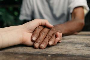 manos del anciano y una mano de mujer en la mesa de madera a la luz del sol foto