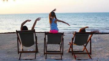 weinig meisjes en moeder zittend Aan strand stoelen Bij zonsondergang video