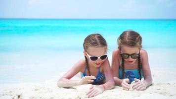 Adorable little kids play with sand on the white beach. Two girls have fun on summer holidays video