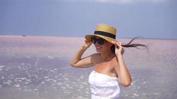 mujer con sombrero camina sobre un lago salado rosa en un día soleado de verano. video