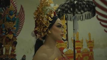 uma mulher balinesa glamorosa em uma fantasia de ouro em pé entre o portão de Bali video