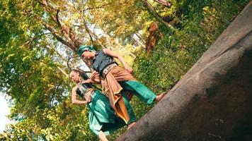 an Asian woman and man are dancing together on a rock while wearing green clothes in the middle of a forest video
