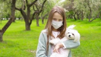 Little girl with dog wearing protective medical mask for prevent virus outdoors in the park video