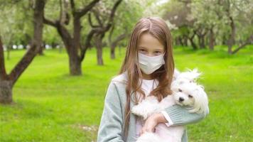 liten flicka med hund bär skyddande medicinsk mask för förhindra virus utomhus i de parkera video