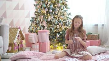 Adorable little girl sitting near the tree and making paper snow-flakes. Room decorated. video