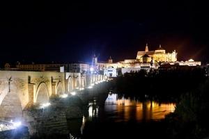 View of the Roman Bridge, a stone bridge that spans the river Guadalquivir in Cordoba, Spain at night. photo