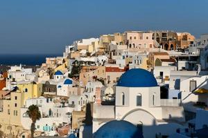 Charming view Oia village on Santorini island, Greece. Traditional famous blue dome church over the Caldera in Aegean sea. Traditional blue and white Cyclades architecture. photo