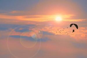 silhouette paramotor flying follow birds and sunset cloud background with fog over on the top mountain photo