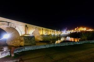 View of the Roman Bridge, a stone bridge that spans the river Guadalquivir in Cordoba, Spain at night. photo