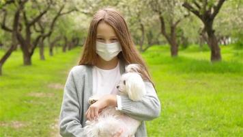 weinig meisje met hond vervelend beschermend medisch masker voor voorkomen virus buitenshuis in de park video