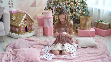 Adorable little girl sitting near the tree and making paper snow-flakes. Room decorated. video