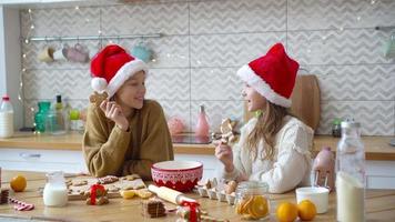 niñas pequeñas haciendo casa de pan de jengibre de navidad en la chimenea en la sala de estar decorada.