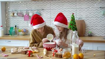 Little girls making Christmas gingerbread house at fireplace in decorated living room.