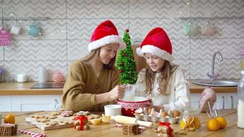 niñas pequeñas haciendo casa de pan de jengibre de navidad en la chimenea en la sala de estar decorada.