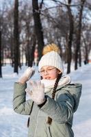 A girl in warm clothes wants to throw a snowball in a winter park. Outdoor games. photo