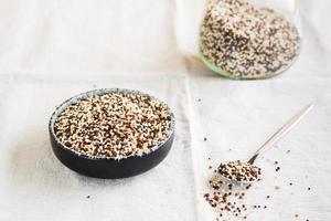 Mix of raw white, red and black quinoa in a bowl and in a spoon on a cloth. Healthy gluten free food photo