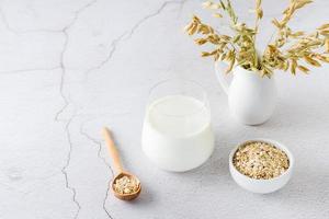 Oat milk in a glass, oatmeal in a bowl and ears in a jug on a light table. Alternative plant food. Copy space photo