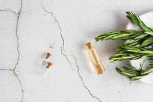 A bottle of rosemary essential oil and herb branches on a plate on the table. Organic aromatic natural remedy. Top view photo