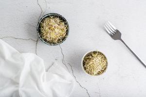 Fresh clover and alfalfa sprouts for food in a bowl on a light table. Detox organic diet. Top view photo