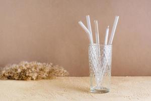 Glass reusable straws for drinks and cleaning brush in a glass on a beige textured background. Sustainable lifestyle. photo
