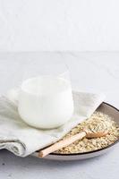 Oat milk in a glass on a plate with dry oatmeal on a light table. Alternative plant food. Vertical view photo