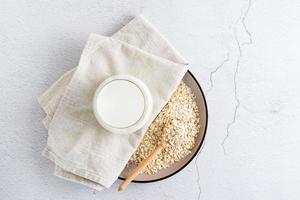 Oat milk in a glass on a plate with dry oatmeal on a light table. Alternative plant food. Top view photo