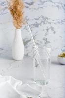 A glass of clean water and a glass straw for drinking on a light table. Diet organic lifestyle. Vertical view photo