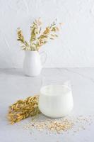 Oat milk in a glass, ears and scattered dry oatmeal on a light table. Alternative plant food. Vertical view photo