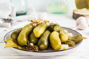 listo para comer en escabeche pepinos en un plato y ingredientes para Cocinando en un de madera mesa. hecho en casa meriendas. foto