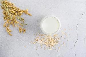 Oat milk in a glass, ears and scattered dry oatmeal on a light table. Alternative plant food. Top view photo