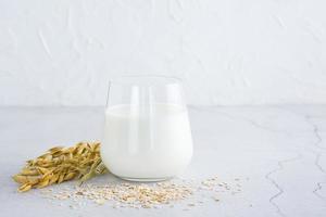 Oat milk in a glass, ears and scattered dry oatmeal on a light table. Alternative plant food. Copy space photo