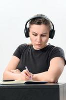 ocupado joven mujer en auriculares trabajando en computadora portátil, haciendo vídeo llamada y haciendo notas en computadora portátil, trabajo y estudiar en línea. foto
