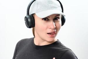 Portrait of a girl on a white background with wireless headphones and a cap on her head, copy space with emotional photo of a girl with headphones.