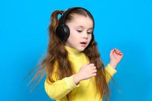 contento pequeño niña con inalámbrico auriculares en un azul antecedentes foto