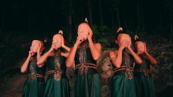 a group of Asian women in green traditional clothes wearing bamboo masks together while standing among the rocks video