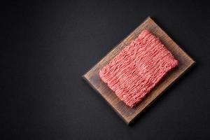 Raw beef or pork mince with salt spices and herbs on a wooden cutting board photo