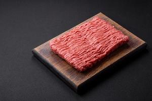 Raw beef or pork mince with salt spices and herbs on a wooden cutting board photo