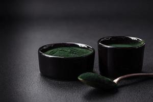 Spice, green color spirulina in the form of powder in a black bowl photo