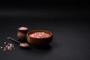 Pink himalayan salt in a wooden bowl on a dark concrete background photo