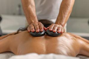 Close rear view of woman having back massage with stones by professional masseur in health spa photo