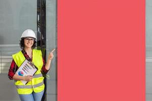 mujer trabajador con un chaleco y casco señalando un rojo póster foto