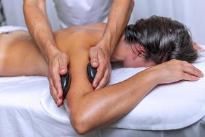 Side view of young woman having arm massage with stones by professional masseur in spa salon photo