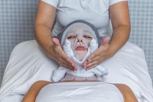 Beautician applying a towel to the face of a woman who is covered with gauze for skin treatment photo