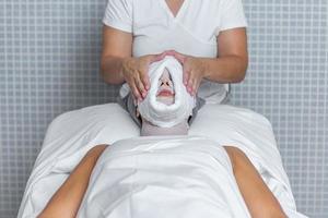 Therapist applying a towel to the face of a woman who is covered with gauze for skin treatment photo