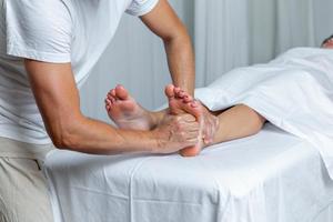 Unrecognizable man applying pressure to foot of woman in reflexology massage at spa photo